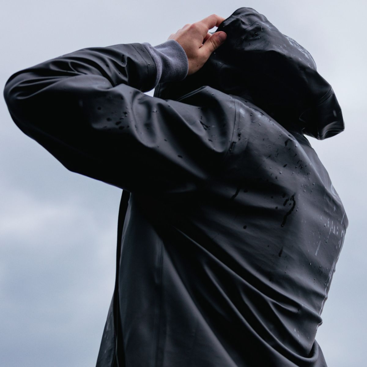 Man wearing a Stockholm raincoat from the Scandinavian brand STUTTERHEIM, standing in heavy rain in a Nordic scenery.